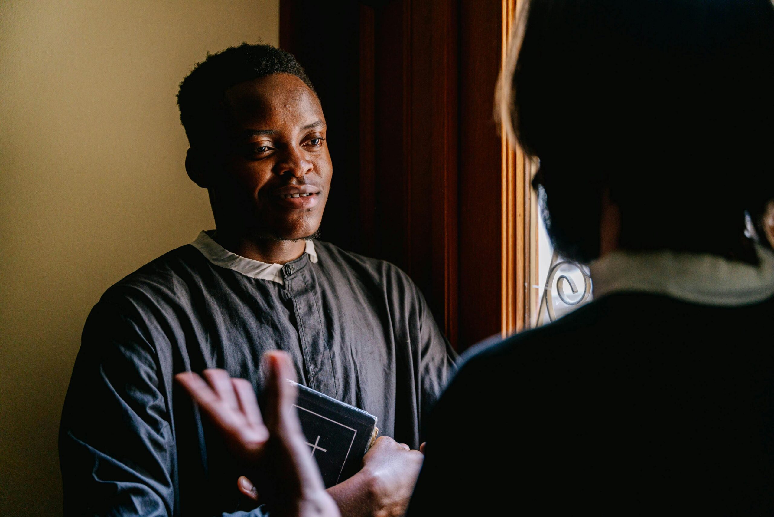 Two seminarians discussing religious teachings with a Bible in hand, bathed in natural light.