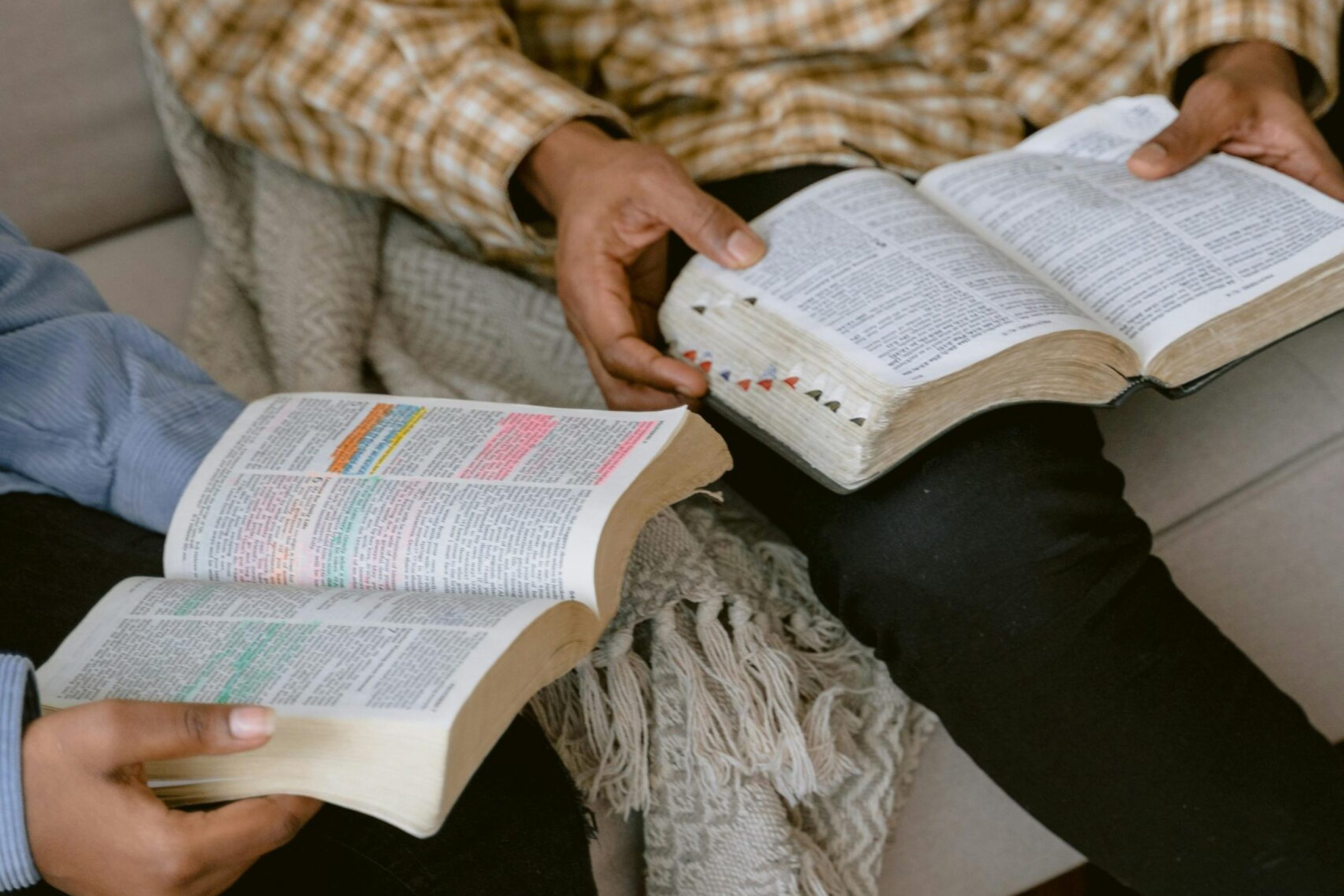Two individuals sitting on a sofa reading and discussing the Bible indoors.